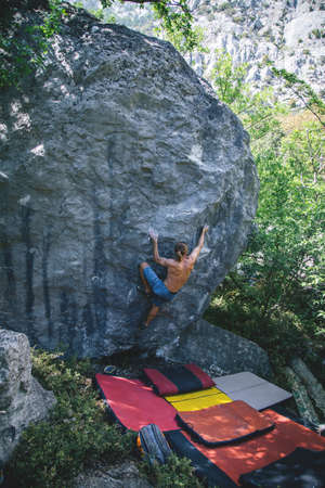Athletic man climbing hard boulder problem in forest using special crash pads. Sport climbing, bouldering. Outdoor.の写真素材