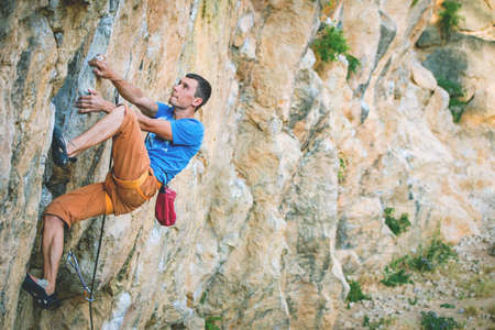 Athletic man climbs a rock in the forest with rope. Sport climbing in Crimea, lead.