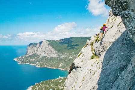 Woman in helmet and special equipment climbing high mountain via ferrata. Crimea.の写真素材