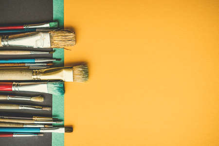 Mass of different paint brusheas on vibrant color paper background.の写真素材