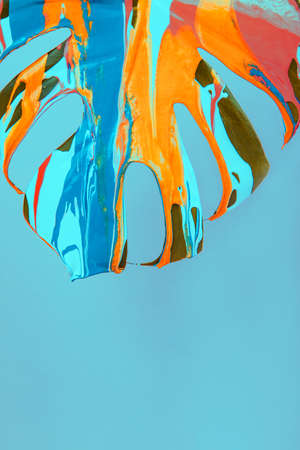 Monstera plant leaf covered with pouring colorful acrylic painting on pink background.の写真素材