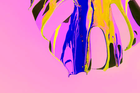 Monstera plant leaf covered with pouring colorful acrylic painting on pink background.の写真素材