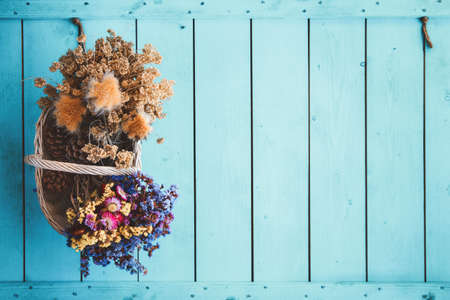 Autumn style basket full of dry flowers bouquets on blue colored wooden background.の写真素材