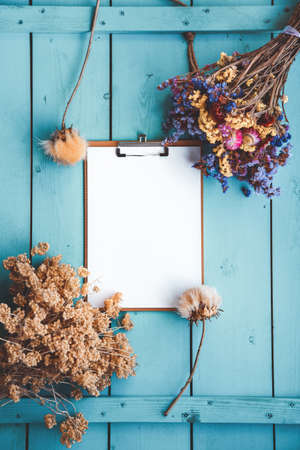 Blank paper, dry flowers and herbs, cones and seed composition autumn style on blue wooden background. Flat lay style.の写真素材