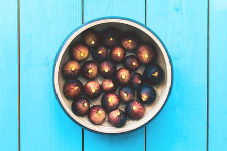 Cropped farme of wooden plate full of ripe figs harvest on a blue wooden table.の写真素材