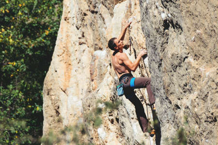Athletic man climbs a rock in the forest with rope. Sport climbing in Crimea, lead.