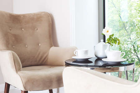Two white ceramics cups and tea cattle with white rose inside on black glass round table and beige...