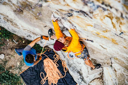 Young woman climbs an overhanging rock  with rope. Sport climbing, lead. Upper view.