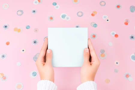 Female hands holding light blue gift box on light pink background covered with confetti.の写真素材