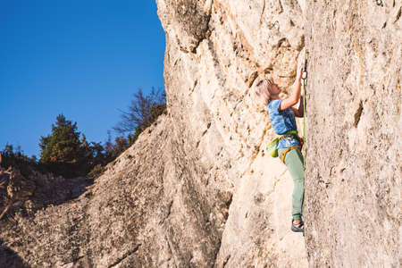 Athletic beautiful blonde hair woman climbs a rock with rope. Sport climbing, lead. Side view. Crimea.の写真素材
