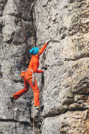 Athletic woman in colorful sportswear climbs a rock with rope. Sport climbing, lead. Side view....