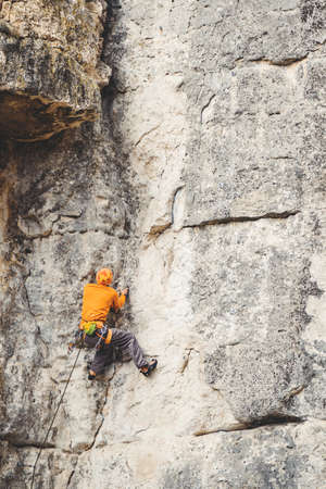 Athletic man climbs very high limestone rock with rope, lead climbing. Sport climbing outdoor.の写真素材