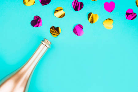 Golden colored bottle of champagne    and splashing out heart shaped confetti on turquoise background. Festive background for projects.の写真素材