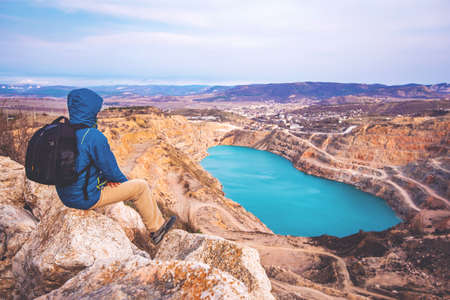 Young man traveller looks at bright blue opencast (lake) standing on the top of a hill. Crimea,...