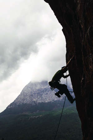 Silhouette of athletic man climbs an overhanging rock with rope, lead climbing in Turkey. Sport...