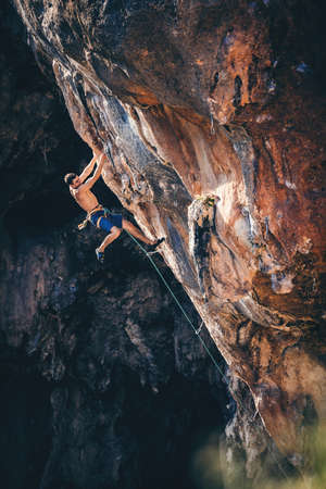 Athletic man climbs very high limestone rock with rope, lead climbing. Sport climbing outdoor.の写真素材