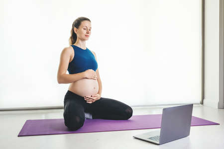Pregnant woman makes yoga practice  on-line class at home. Concept of  staying at home at quarantine...