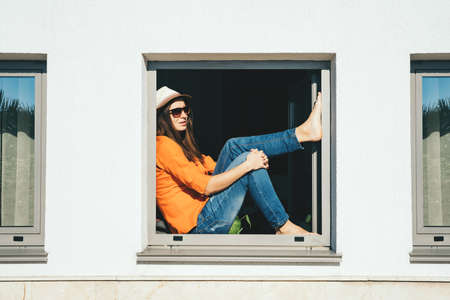 Smiling woman looking out of window staying at home. Self isolation concept.