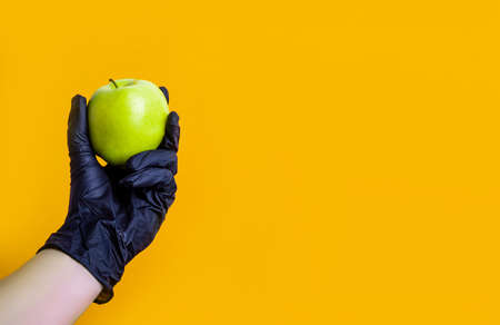 Hand in black protective glove hold green apple. Concept of self protection while virus pandemia.の写真素材
