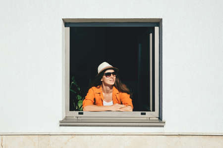 Smiling woman looking out of window staying at homeの写真素材