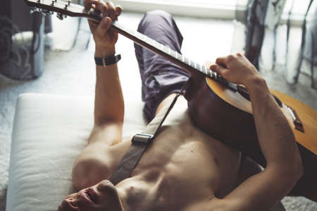 Man laying in a bedroom and plays the guitar while staying at home.の写真素材