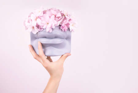 Hand holding bouquet of pink japanese sakura flowers in modern lips shaped vase. Modern art beauty concept.の写真素材