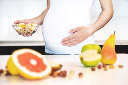 Cropped frame of pregnant woman cooking fruit granola breakfast. Healthy food concept for pregnant woman.の写真素材