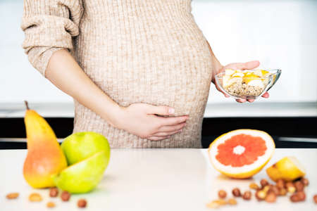 Cropped frame of pregnant woman cooking fruit granola breakfast. Healthy food concept for pregnant...
