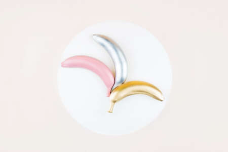 Silver, pink and golden colored bananas on white circle background. Flat lay style, tropic summer visual.の写真素材