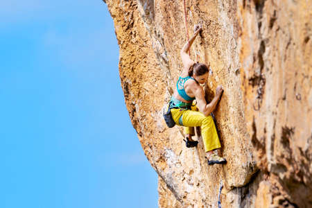 Athletic beautiful woman climbs an overhanging rock with rope, lead climbing. Sport climbing outdoor.の写真素材