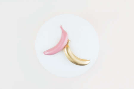 White, pink and golden colored bananas on white circle background. Flat lay style, tropic summer visual.の写真素材