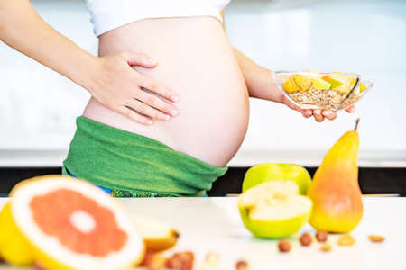 Cropped frame of pregnant woman cooking fruit granola breakfast. Healthy food concept for pregnant woman.の写真素材