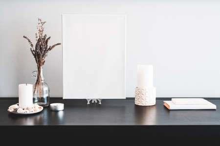 Interior design of room, blank white canvas for artist's mock-up, lips shaped vase with dry flowers bouquet, candles, white books on black table and white wall. Minimalism style.の写真素材