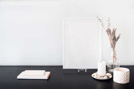 Interior design of room, blank white canvas for artist's mock-up, lips shaped vase with dry flowers bouquet, candles, white books on black table and white wall. Minimalism style.の写真素材