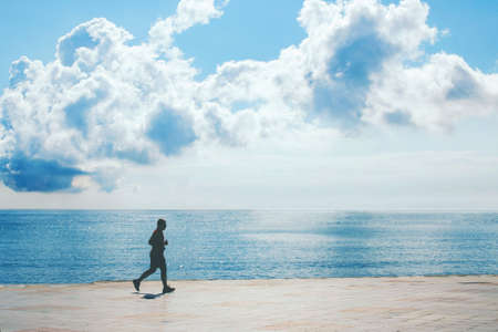 Silhouette of a man jogging along the sea front sunny day. Outdoor sport.の写真素材
