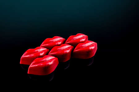 Colorful red lips shaped chocolate candies on isolated black. Holiday gift background, top view.の写真素材