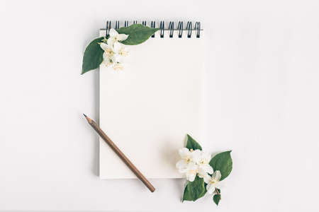 Notepad with pencil and rose flowers top view on white background. Messege or invitation card mock-up concept.の写真素材