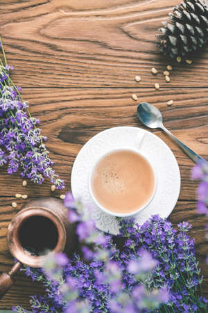 Cup of coffee with foam made in a coffee pot decorated  with lavender flowers, cedar nuts and cown on a wooden tray. Flat lay style.の写真素材