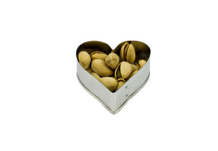 Pistachios in metal heart bowl isolated against white background.の写真素材