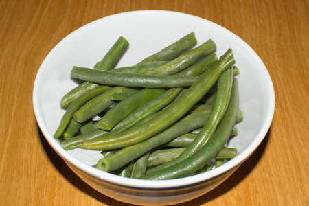 Bowl of cooked green beans over wooden table