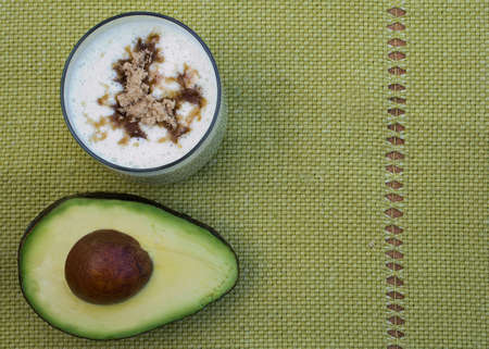 Half an avocado and a cup of avocado smoothie, Brazilian style, on green cloth, photographed from aboveの写真素材