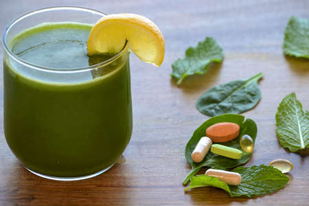 Green detox smoothie and dietary supplements on wooden table