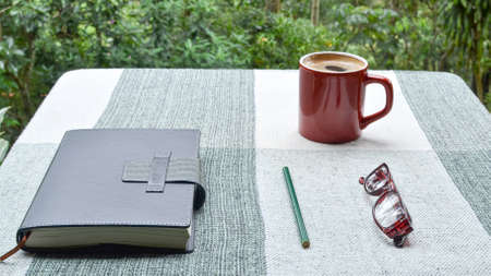 Journal, pencil, readers, and cup of coffee on table in a tropical setting