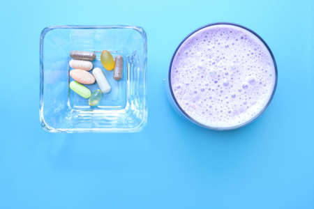 A container with dietary supplements beside a cup of smoothie on blue backgroundの写真素材
