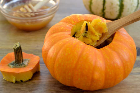 Two baked mini-pumpkins stuffed with spiced pumpkin puree, served with honey, on green dishcloth and wooden table, viewed from above- seasonal food conceptの写真素材