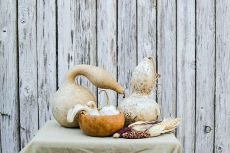 Abstract still life displaying dried gourds and indian corn on tan tablecloth against wooden backgroundの写真素材