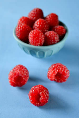 Abstract red and blue composition showing intense red raspberries in blue bowl on blue background, with three raspberries in front, forming a triangleの写真素材