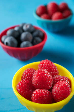 Blackberries, blueberries and raspberries in colorful bowls on blue background, lined upの写真素材