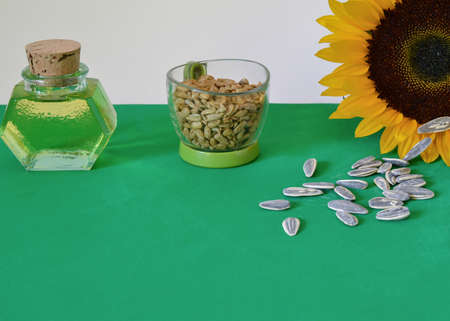 Sunflower and its edible products: shelled and unshelled sunflower seeds and oil, front view; on green surfaceの写真素材