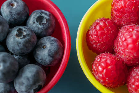 Blackberries and raspberries in colorful bowls cut in half in the frame, on blue backgroundの写真素材